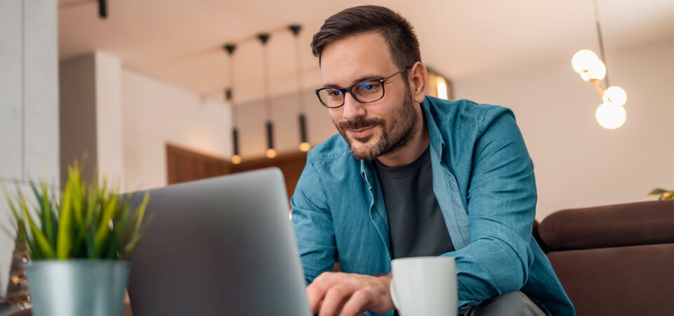 Mies käyttää kannettavaa tietokonetta olohuoneessa hakeakseen lainaa verkossa.