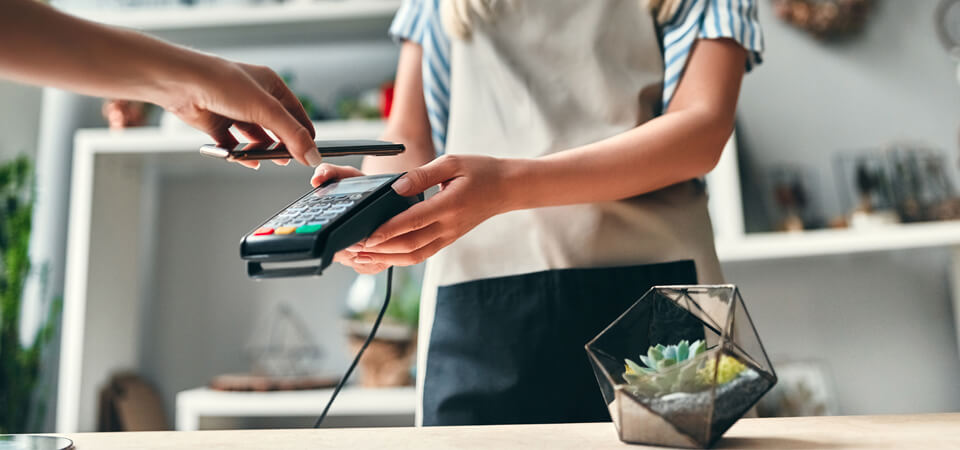 Asiakas maksaa ostoksen puhelimella lähimaksulla myymälän kassalla; myyjä ojentaa maksupäätteen.